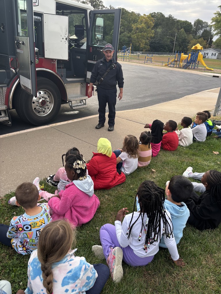 Kindergarten students surrounding and exploring a red fire truck with  firefighters standing nearby during a visit from the East Moline Fire Department.