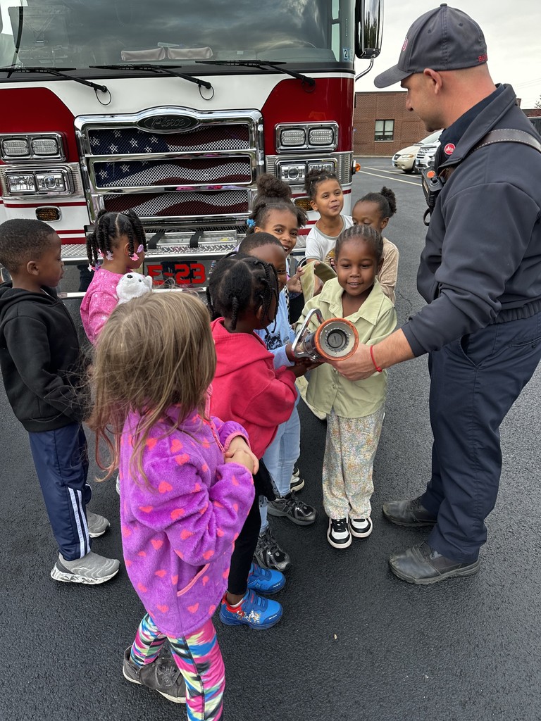 Kindergarten students surrounding and exploring a red fire truck with  firefighters standing nearby during a visit from the East Moline Fire Department.