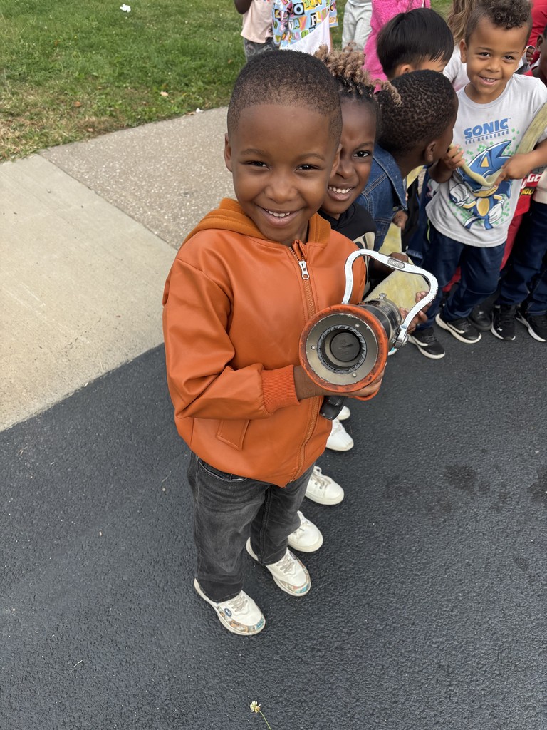 Kindergarten students surrounding and exploring a red fire truck with  firefighters standing nearby during a visit from the East Moline Fire Department.