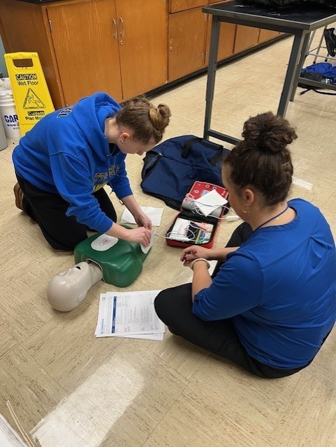 an instructor watching a student practice CPR on a dummy