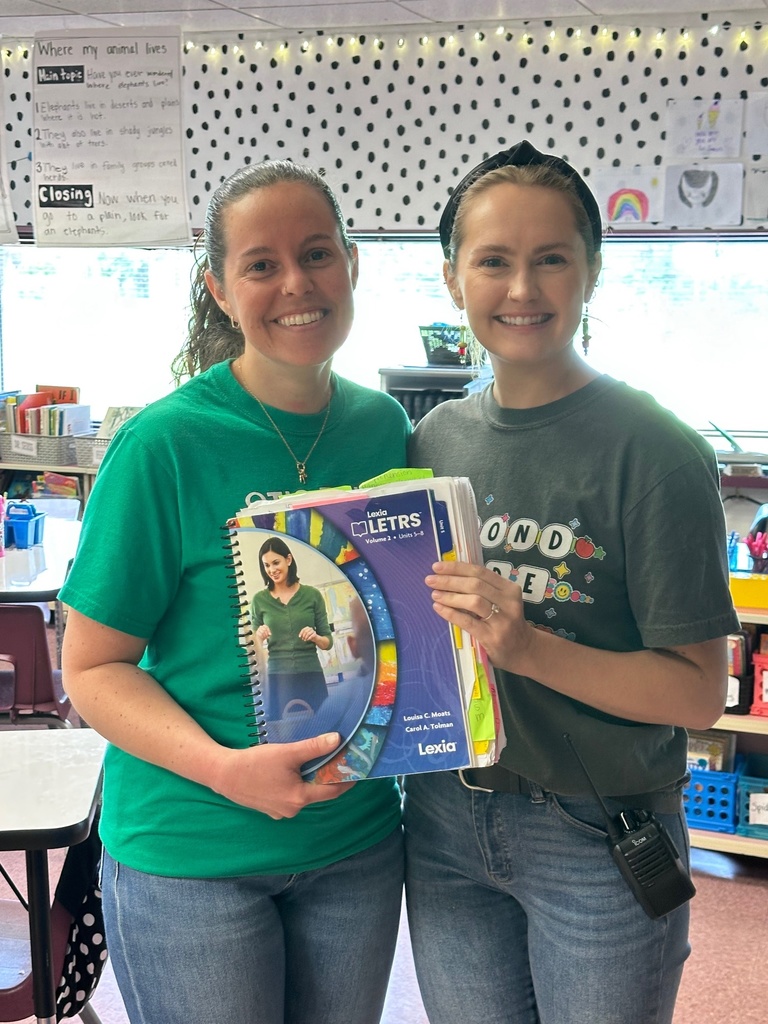 two women standing and displaying a curriculum book