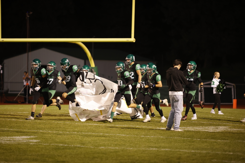 football players on a football field running through a paper banner