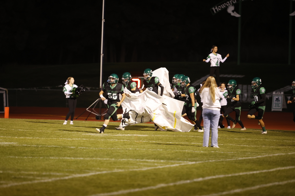 football players on a football field running through a paper banner