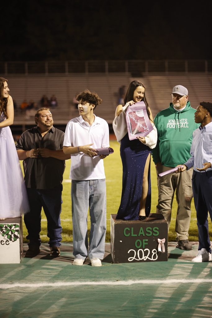 students and adults dressed formally on podiums holding congrats posters