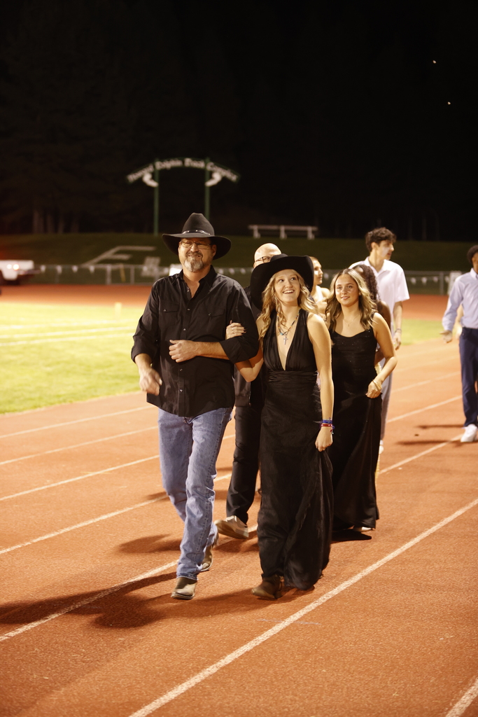 a father and daughter in formal attire smiling while walking on a track and field track
