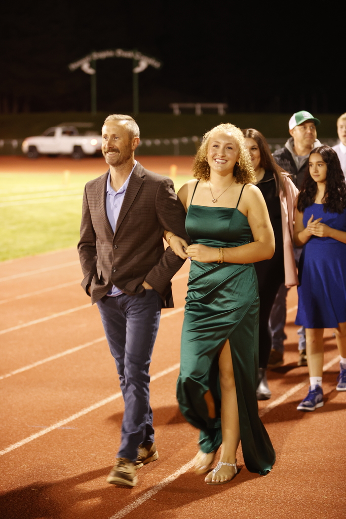 a father and daughter in formal attire smiling while walking on a track and field track
