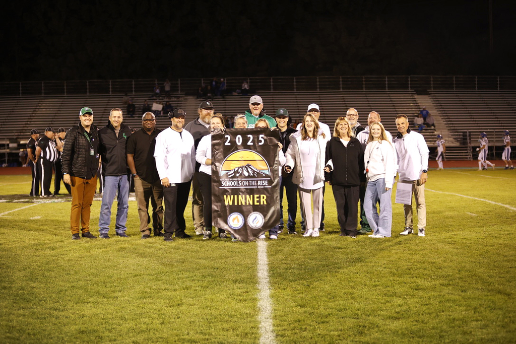 evhs staff gathering on a football field with a schools on the rise banner in celebration of their recognition