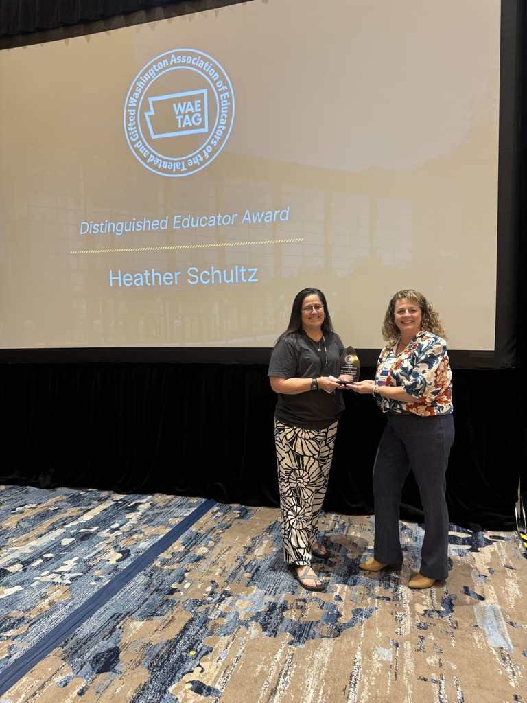 two women standing side by side in front of a projection screen holding a glass award.