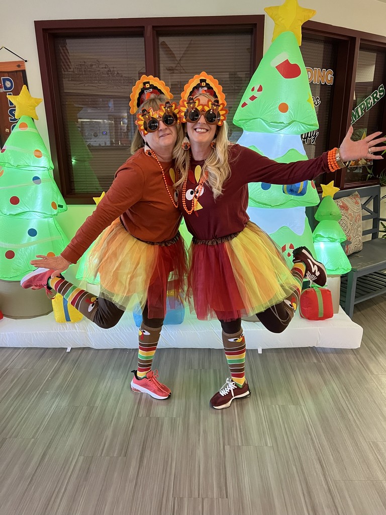 two women in front of blow up christmas trees wearing thanksgiving outfits