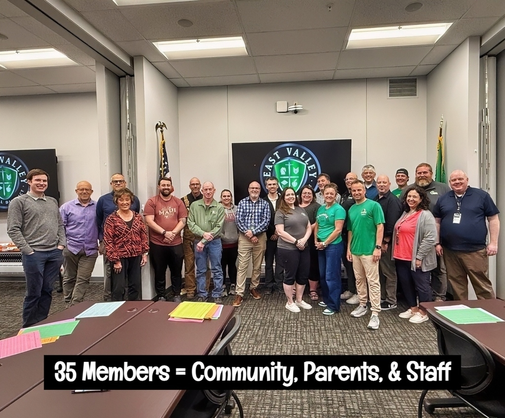 A group of 35 people in various colored shirts and pants stands in a room with tables.