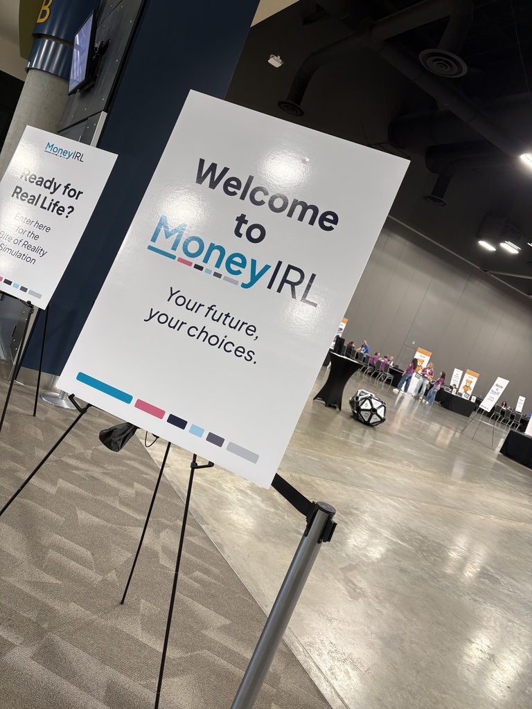 Two white signs on stands, one reading "Welcome to MoneyIRL" and the other partially visible, in a large, empty, brightly lit space.