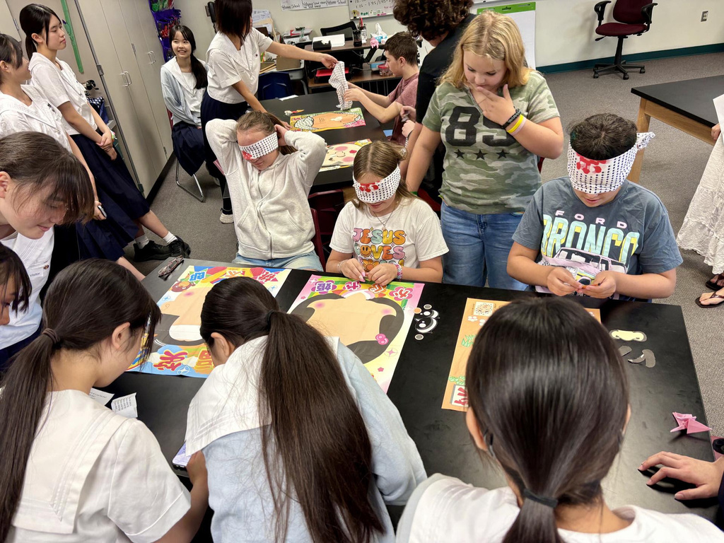 A group of students wearing blindfolds work on projects at tables in a classroom.