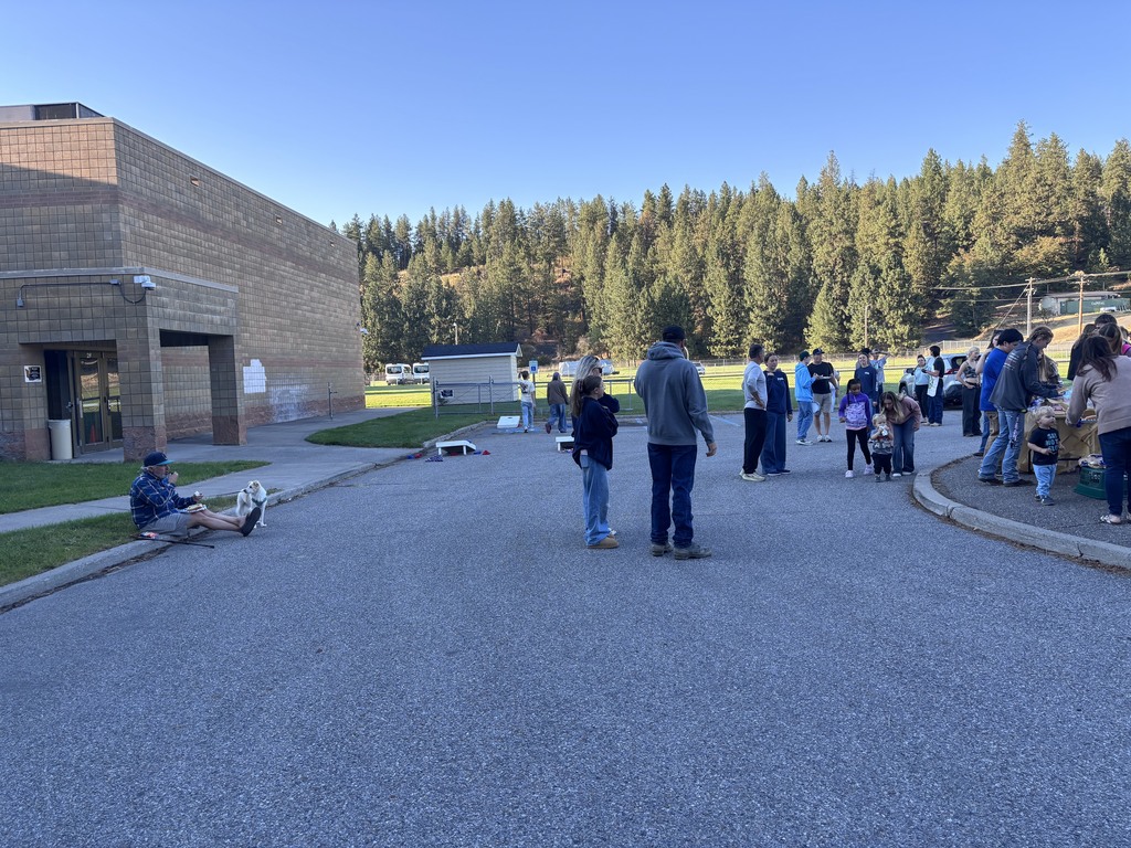 People gather around a school entrance. Trees and a building are in the background.