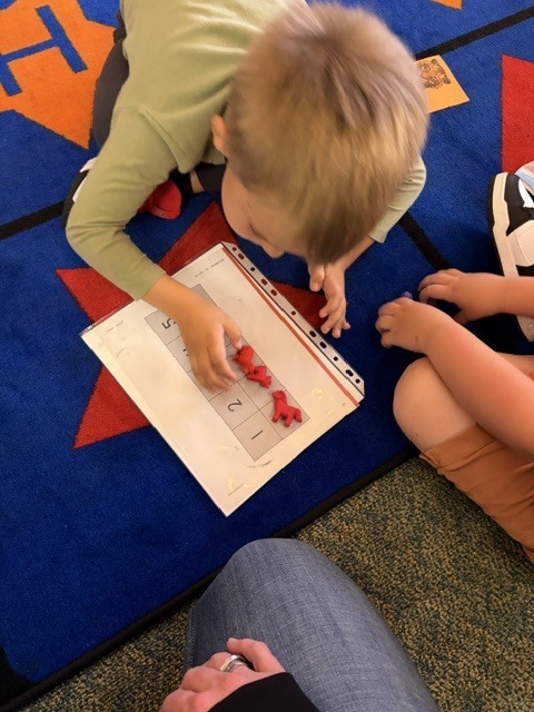 Child wearing green shirt bends over table to count red objects on a page.
