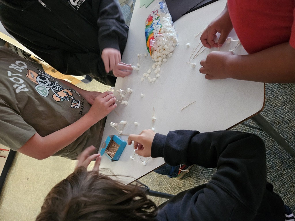 Four individuals work together at a table with a white top, each holding a stick with white objects.