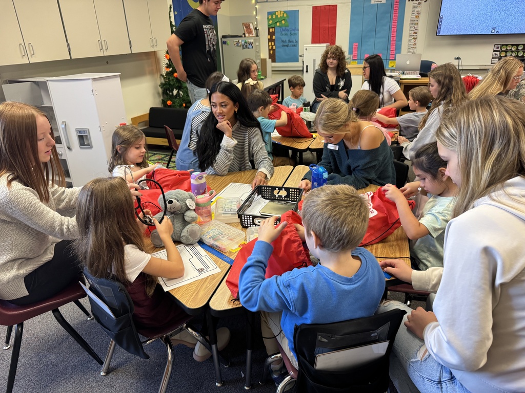 Group of adults and children seated at tables in a classroom. People are working on craft projects.