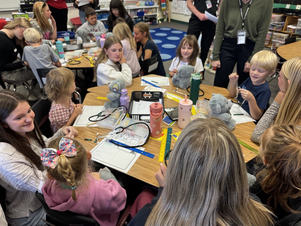 Group of children seated around a table with craft materials, engaged in an activity with an adult.
