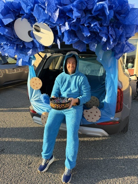Person dressed in blue, holding a box with cookies, seated in the open trunk of a vehicle.