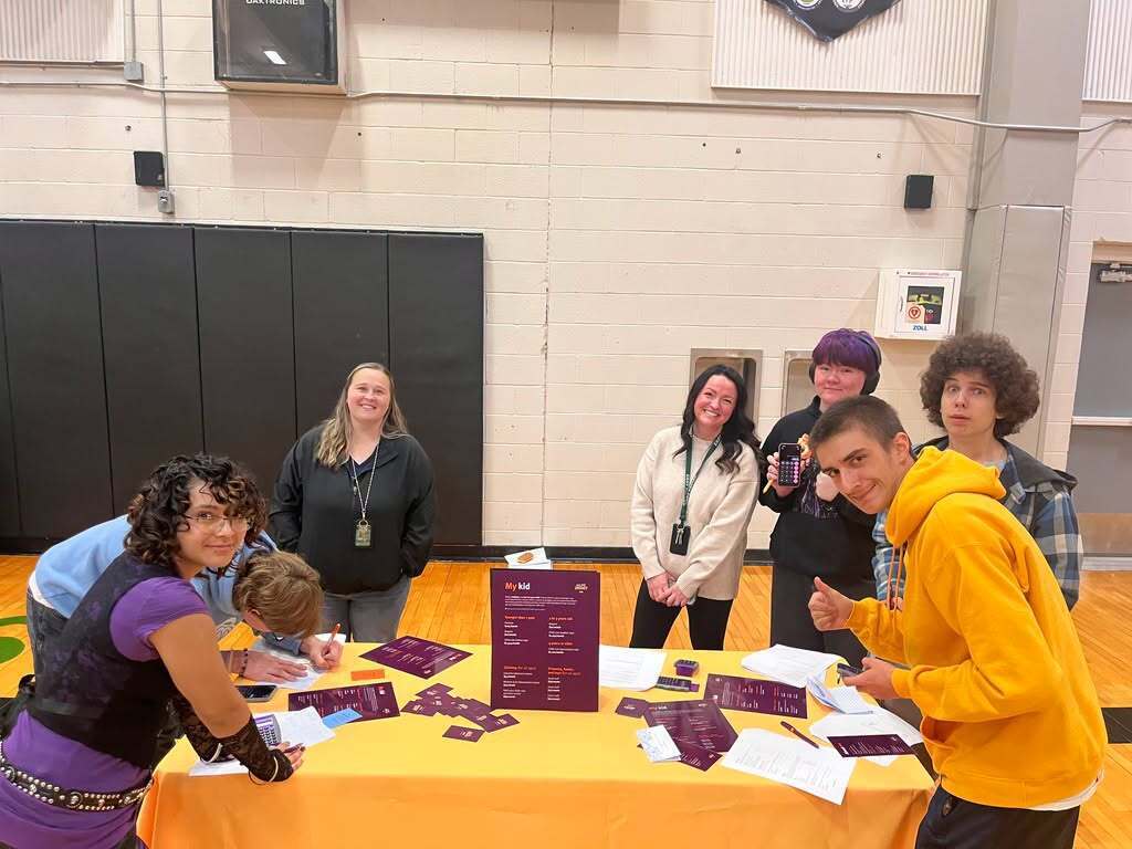 People standing around a table with yellow tablecloth. Papers and cards are on the table.