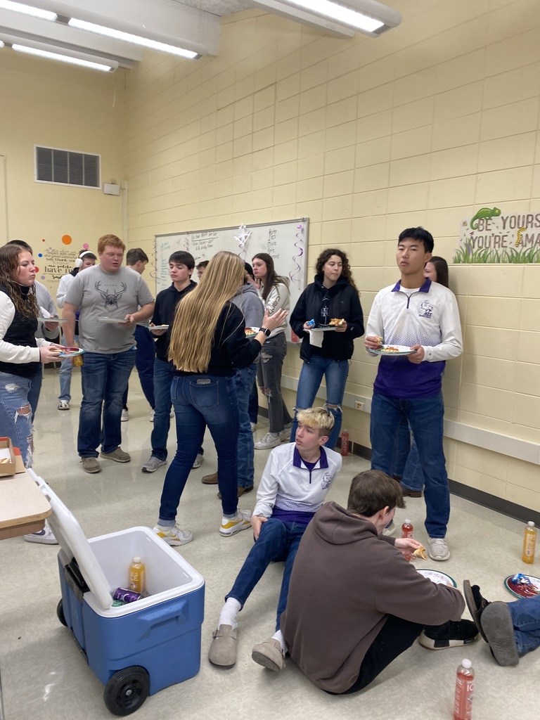 high school students sitting and standing with paper plates full of pizza