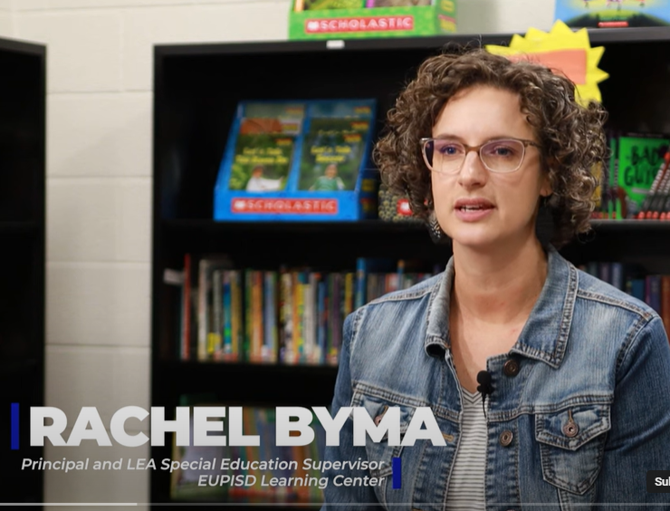 Principal Rachel Byma seated in front of library books on shelves