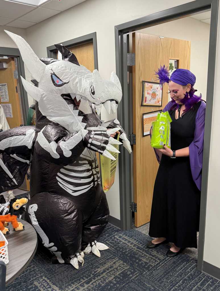 A student in a blowup dinosaur skeleton costume trick or treats from a staff member in a fortune teller costume. 