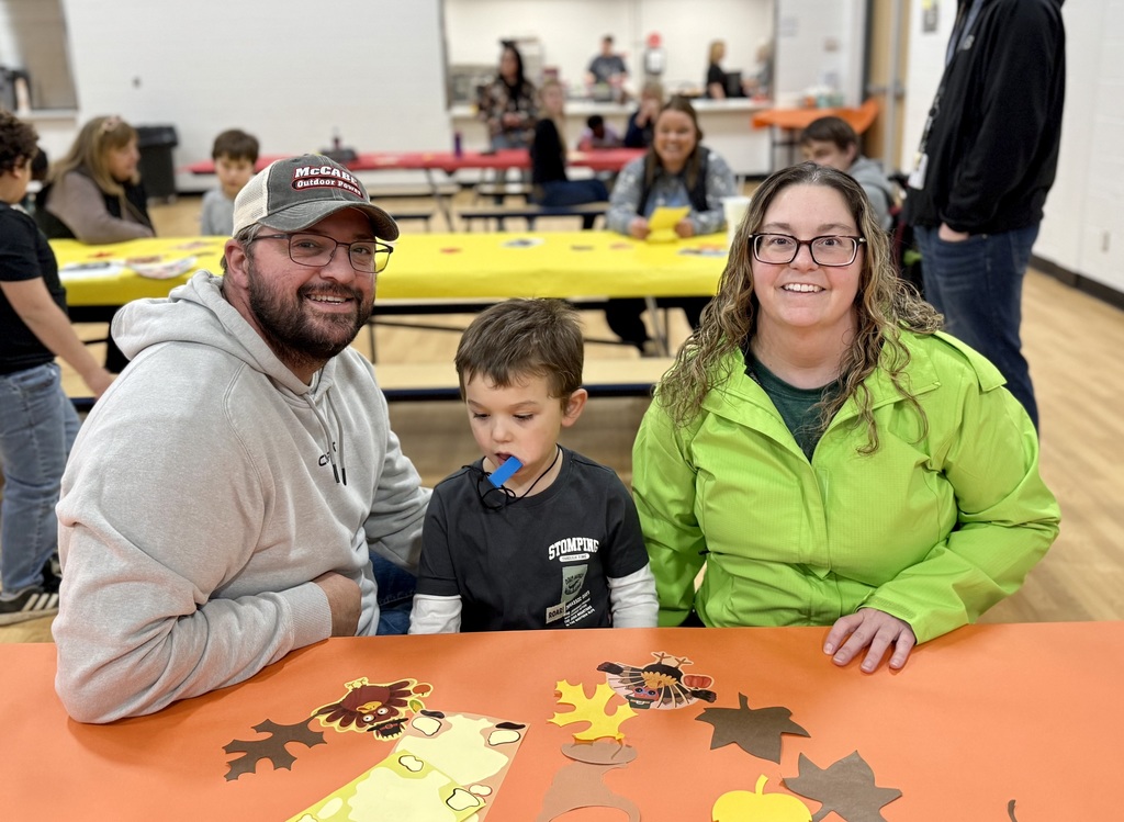 Two adults smiling sit with a young student in between them.