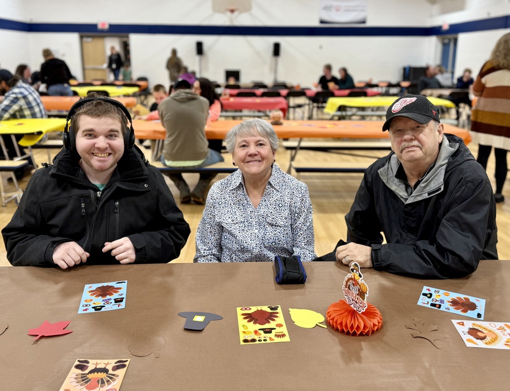 A smiling student and two adults sit at a festively decorated table.