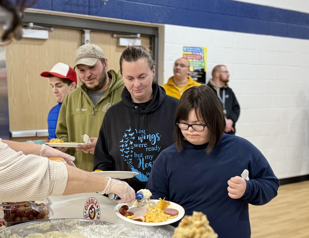 Two adults and a student getting Thanksgiving foods piled on their plates in the serving line.