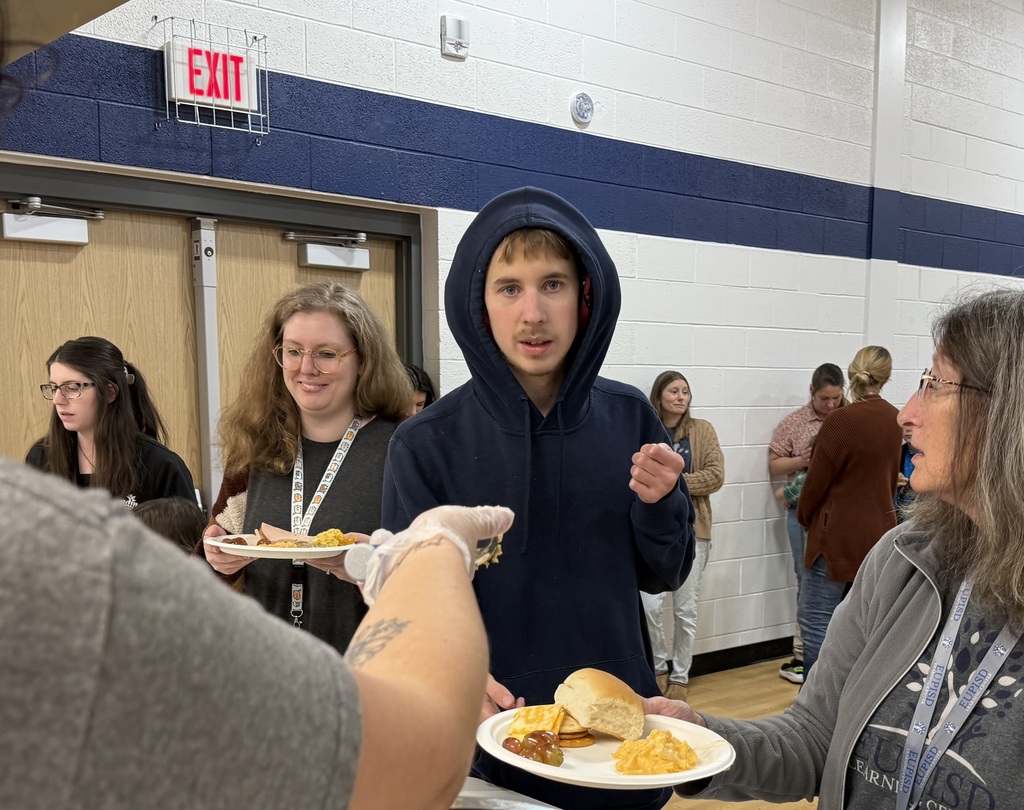 A staff member holds a plate for a student while staff place food on it.