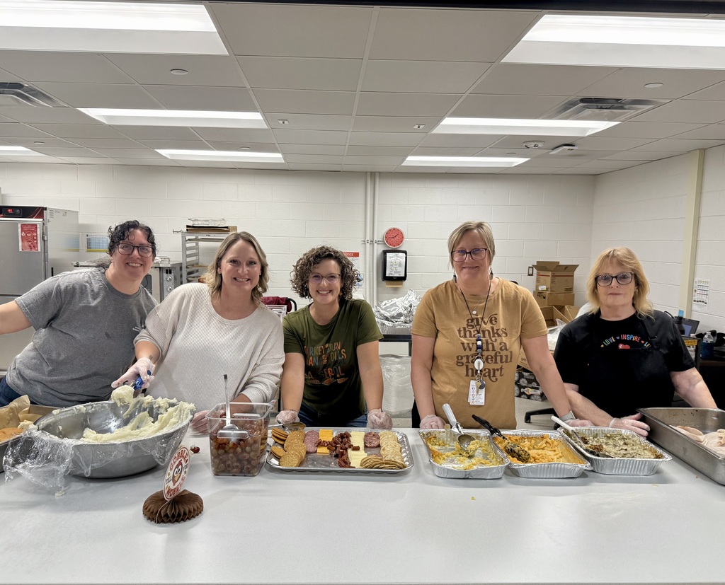 The smiling kitchen crew. Five women stand in front of trays of food - crackers and cheese, green bean casserole, mashed potatoes, and turkey.
