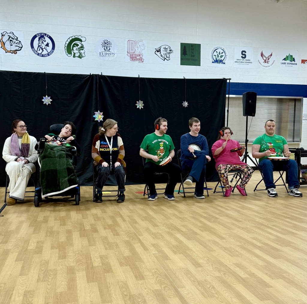 A row of students sit in a line. Each has a small drum and drumstick. 