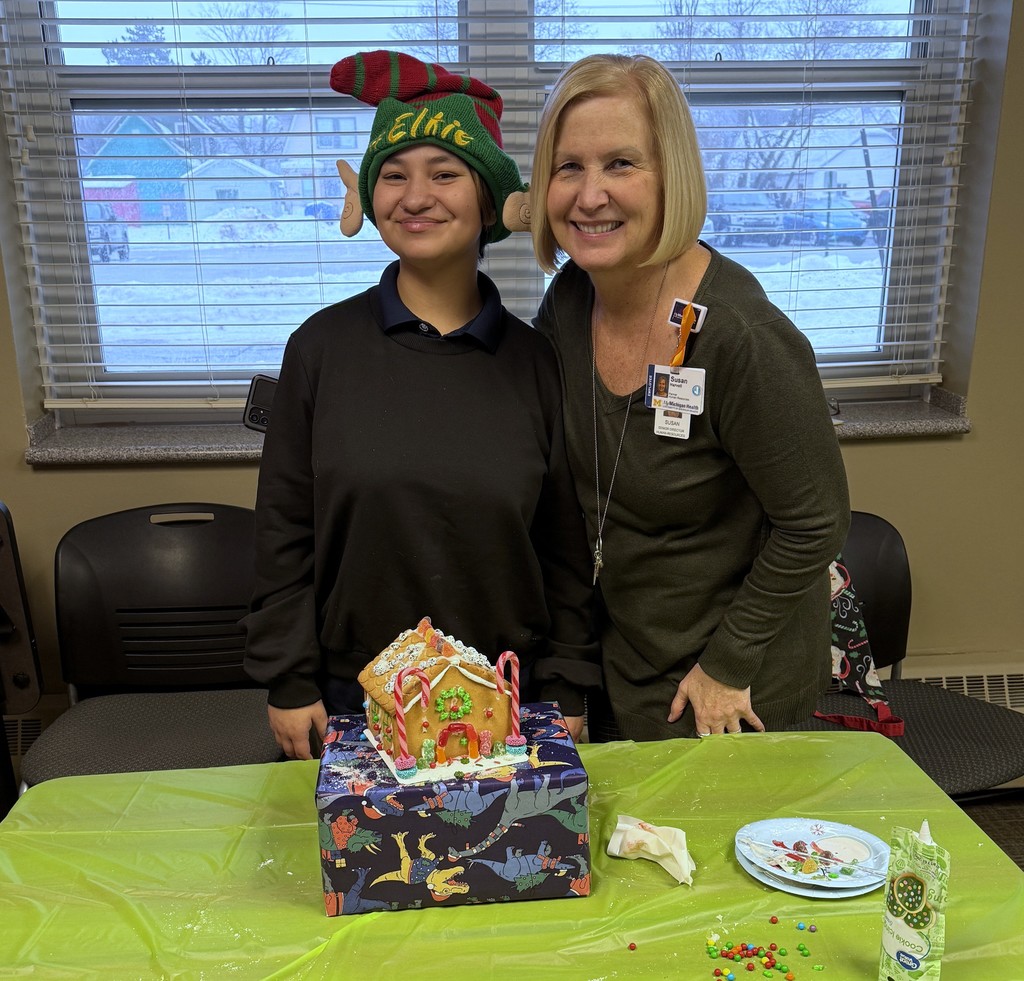 An intern and a staff member smile for the camera, posing with their gingerbread house. 