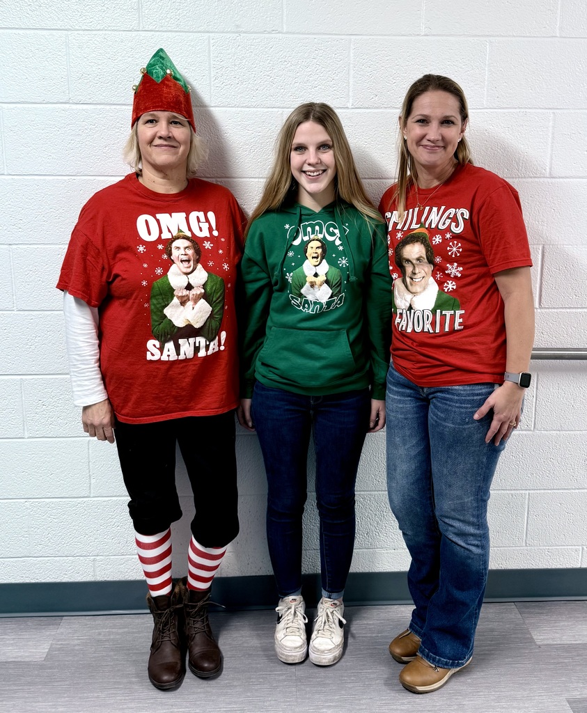 Three smiling staff pose for the camera. They are all wearing "Elf" movie shirts. 
