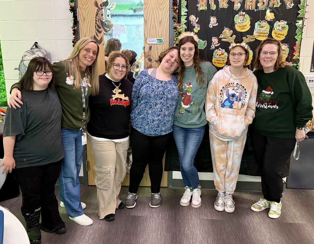 Group photo of staff and students smiling for the camera. There is a classroom in the background. 