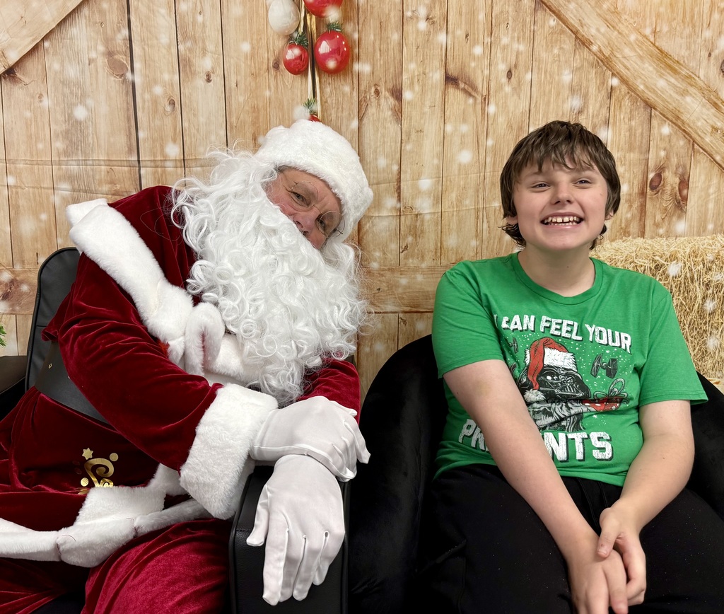 Santa and a student smile for the camera. The student has a holiday Star Wars t-shirt on. 