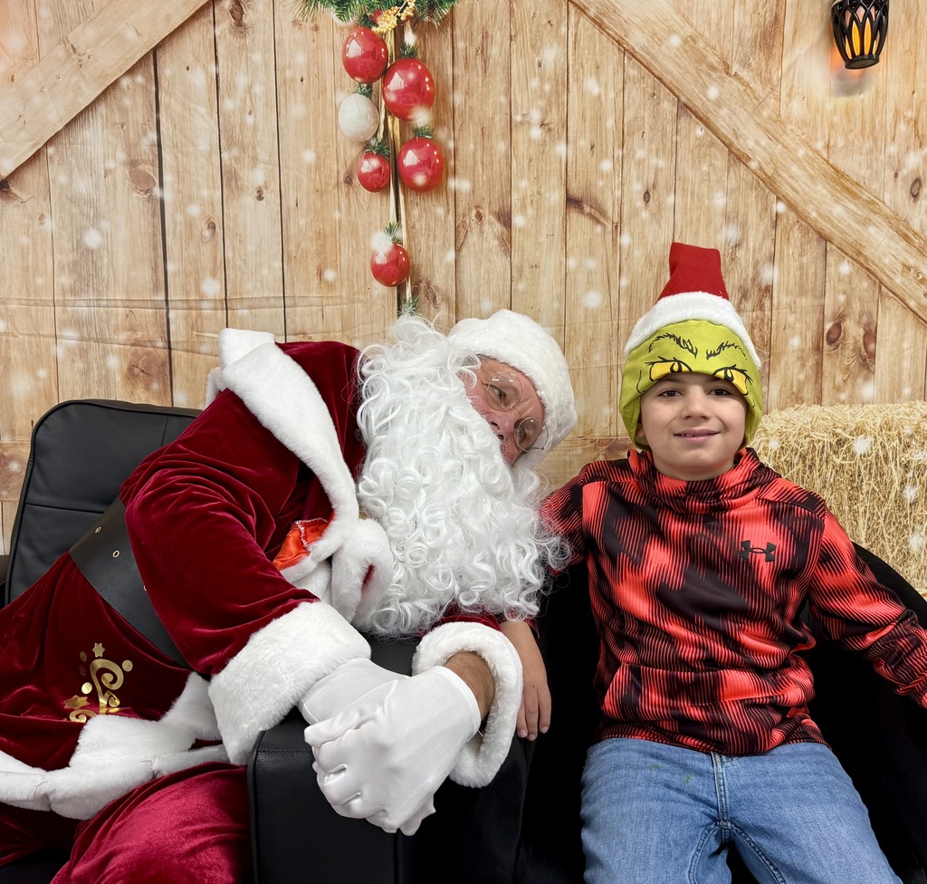 Santa and a smiling student pose for the camera. The student has a "Grinch" hat on. 