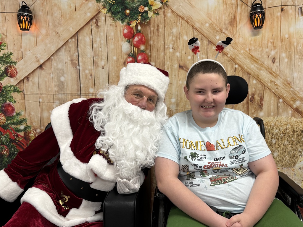 Santa and a student smile for the camera. The student has a holiday "Home Alone"  t-shirt on. 