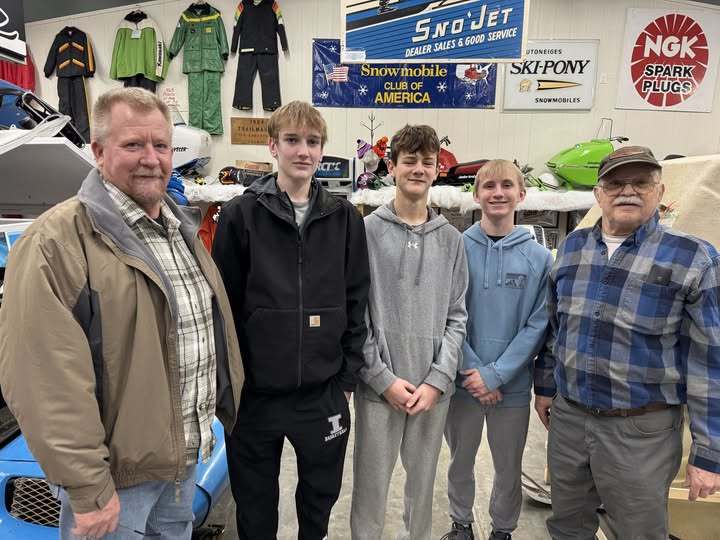 three teenage boy CTE students with two men, members of the snowmobile museum.