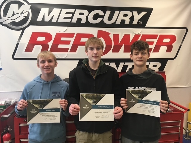 three teenage boy students holding up certificates with the words mercury repower in the background. 