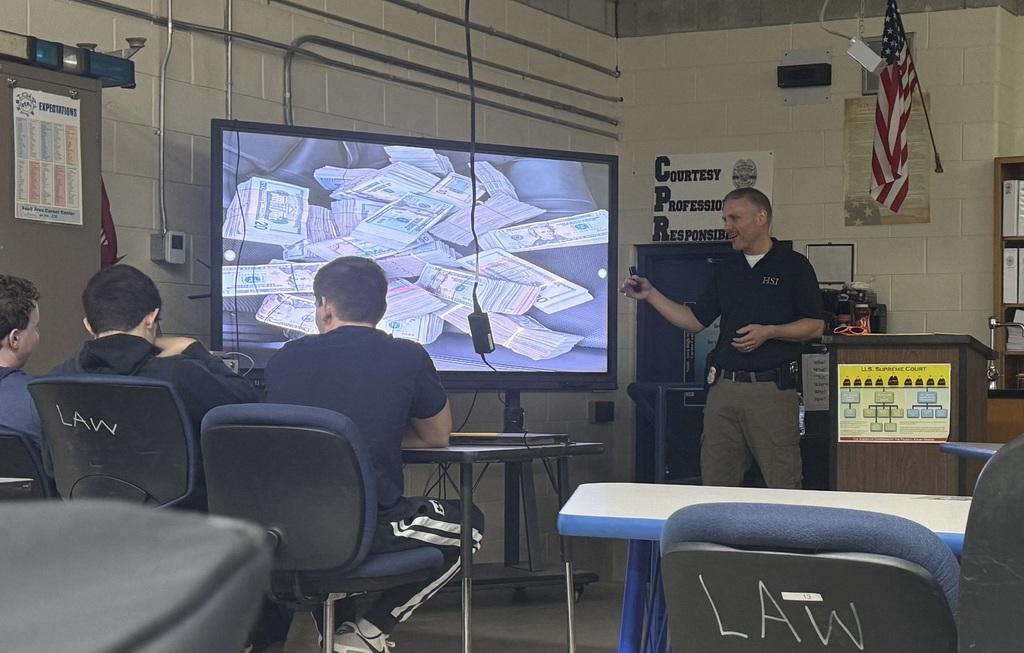 students receiving a presentation from one male presenter, with money shown on the screen 