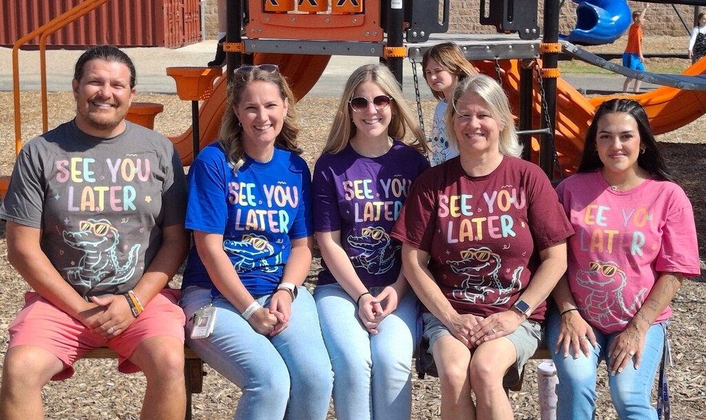 A group smiling teachers pose for a photo on a sunny playground. 