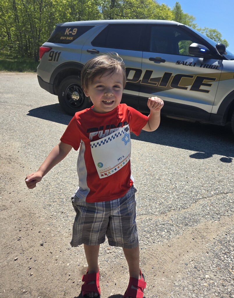 A young student smiles in front of a law enforcement vehicle. 