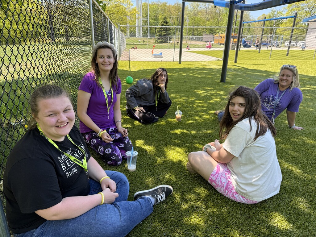 A group of smiling students sit in a circle on the playground. 