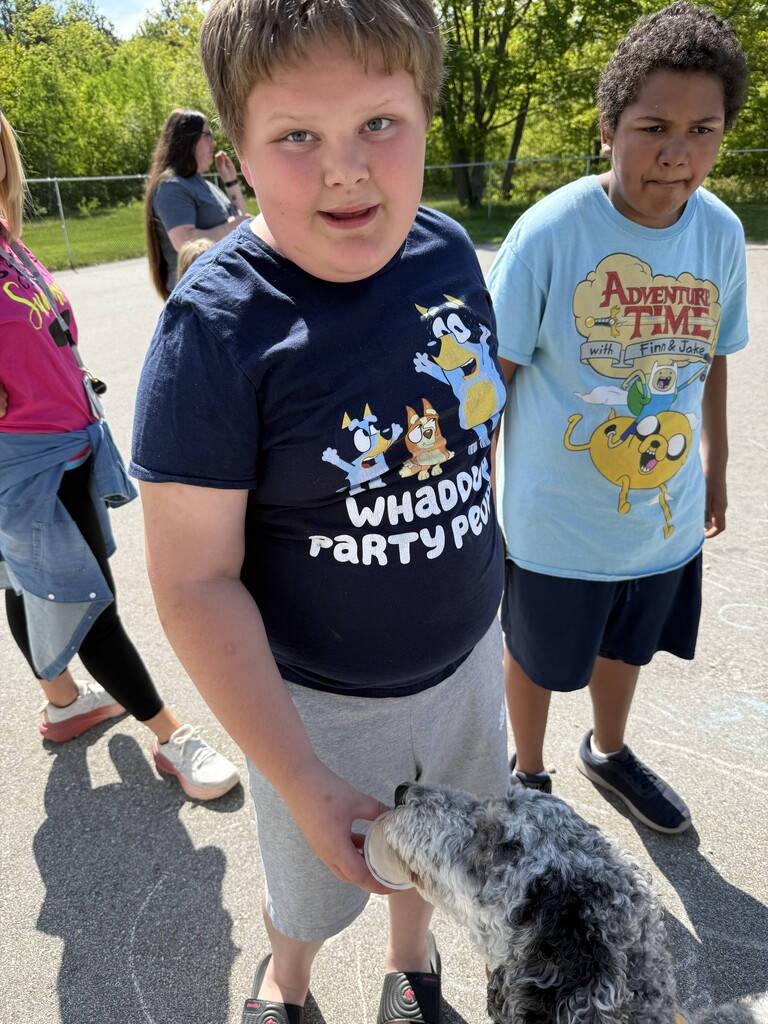Two students stand smiling on the concrete next to the playground. 