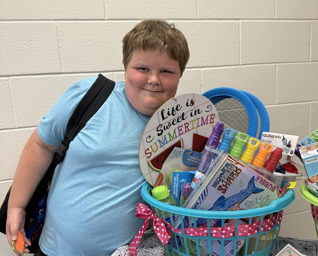 A student smiles next to a prize basket full of colordul summer activities. 