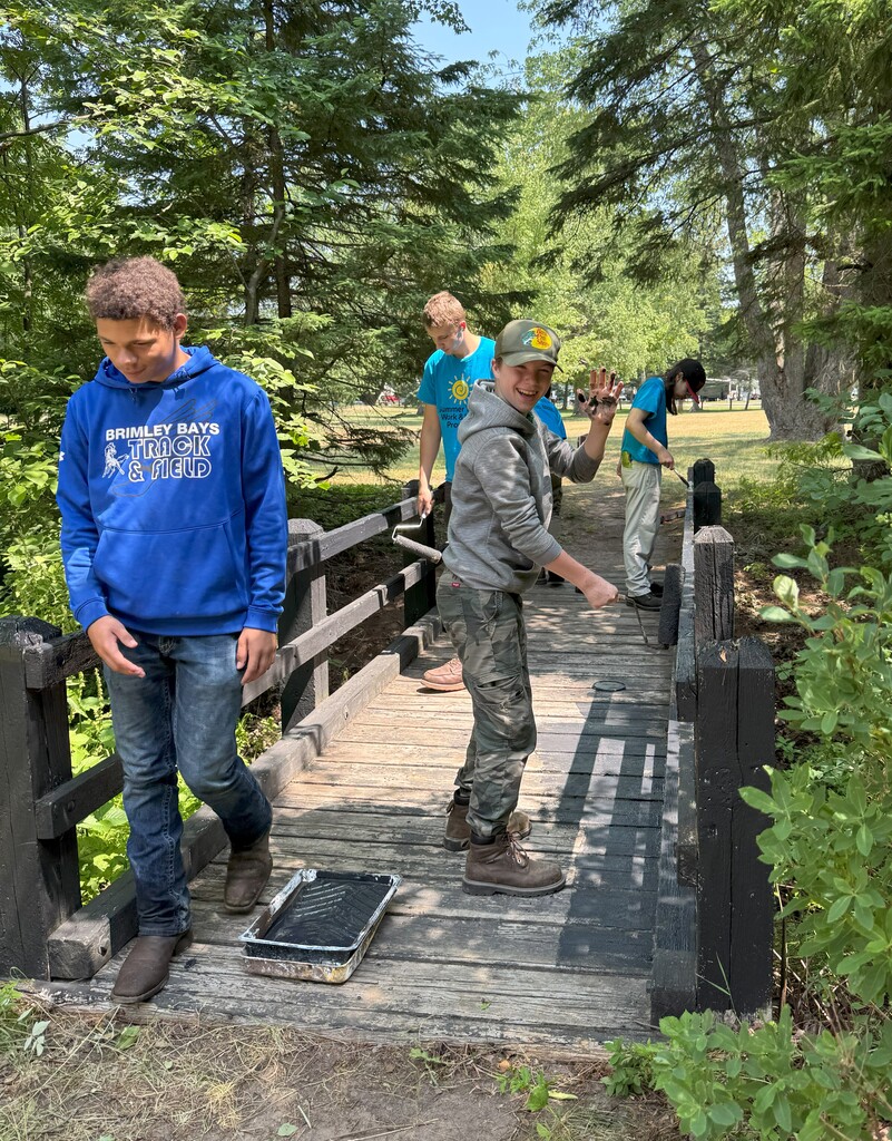 Four young people work to pain a wooden bridge with black paint.