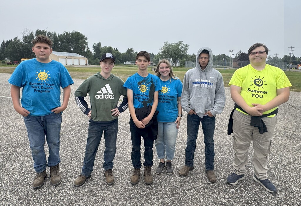 A group of people line up for a photo. Several are wearing Summer Youth Work & Learn t-shrits.