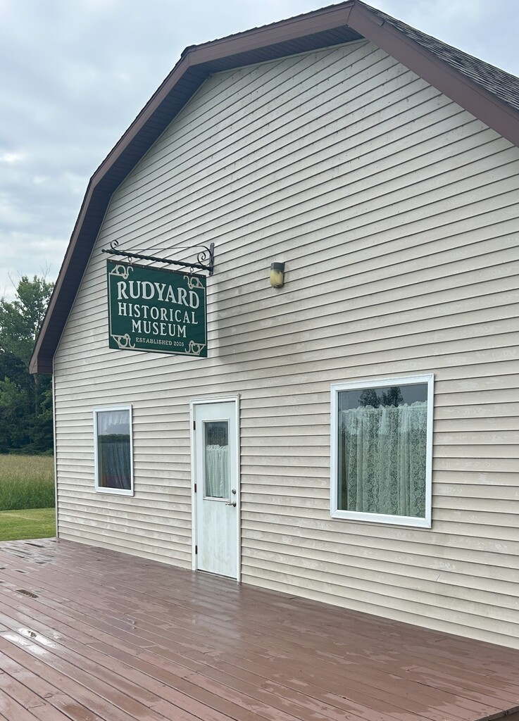 A tan building with a sign on it that reads "Rudyard Historical Society."