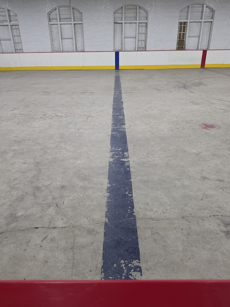 A long blue stripe on the concrete of a rink is badly paeeling.